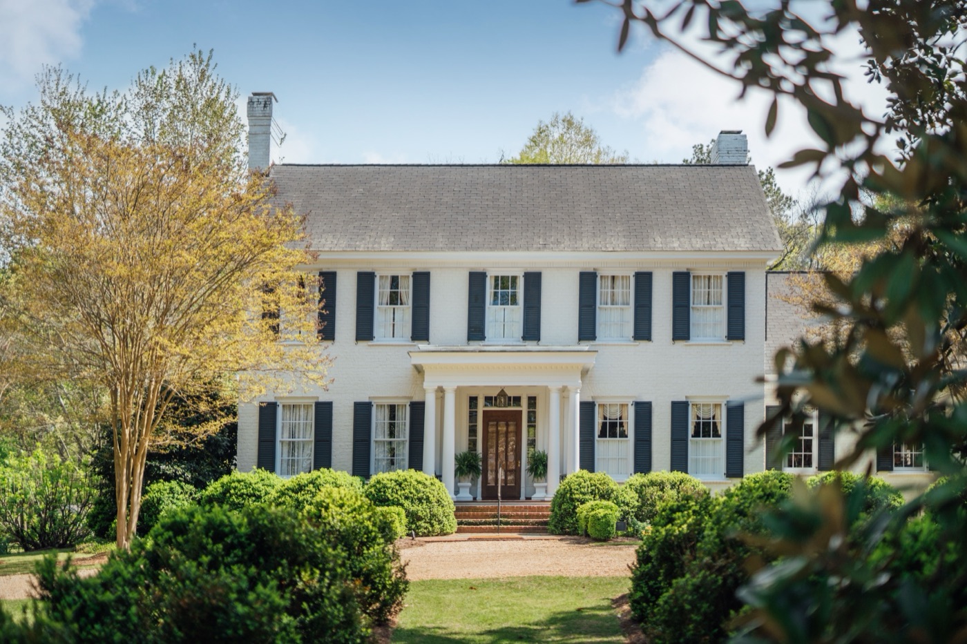 A white two-story colonial house with dark shutters and a columned entry