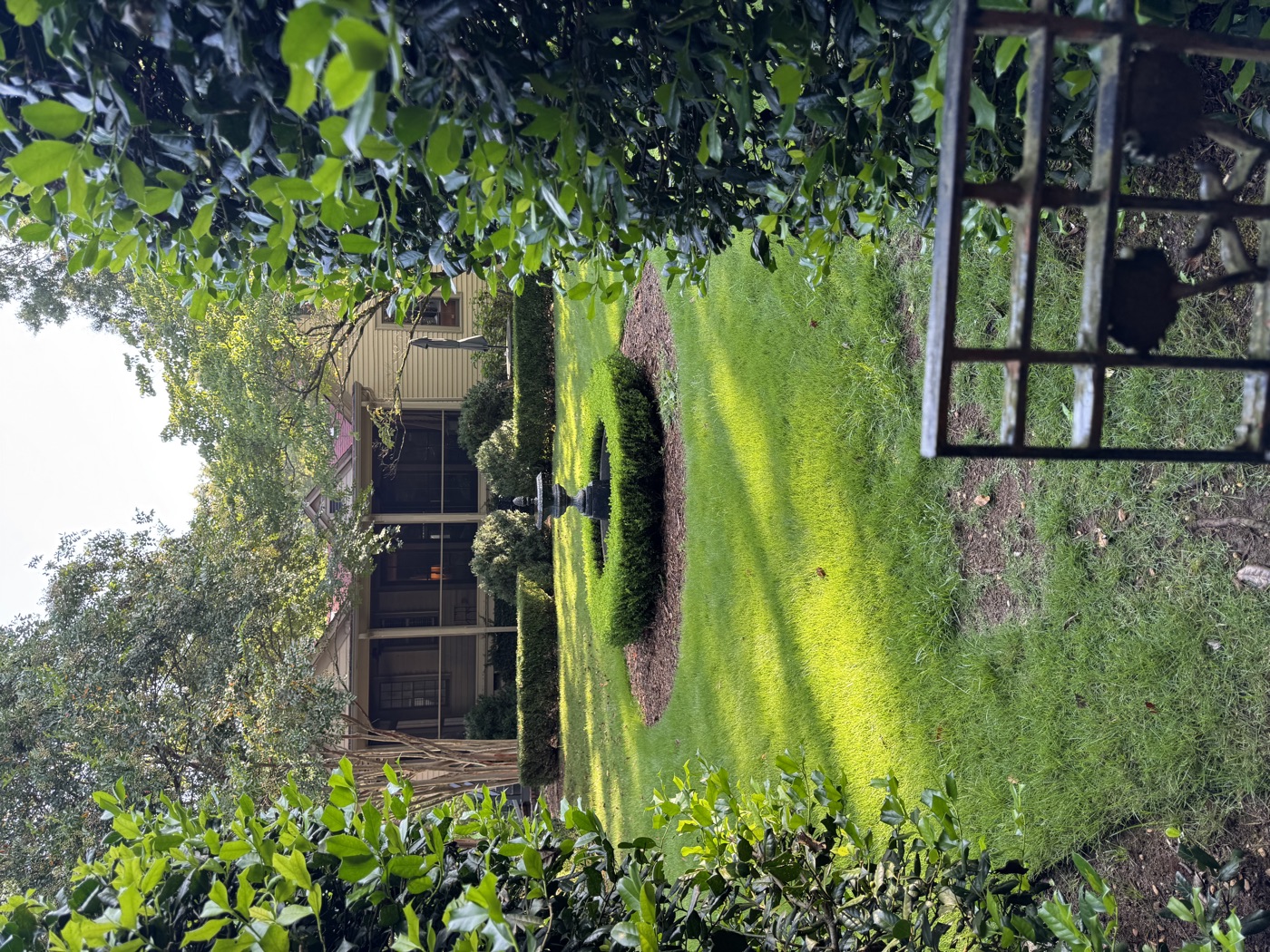 A walled garden with a fountain in a boxwood circle, seen through an iron gate